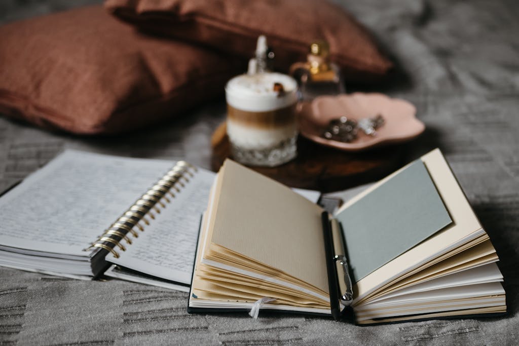 A cozy indoor workspace featuring open DIY gratitude journals and a cup of frothy coffee on a soft textile background.