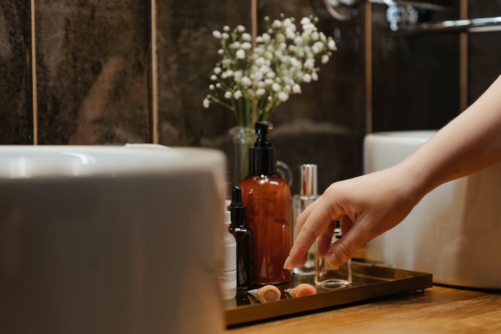 A stylish bathroom scene forfeaturing cosmetics and skincare products on a tray with a hand reaching for them.