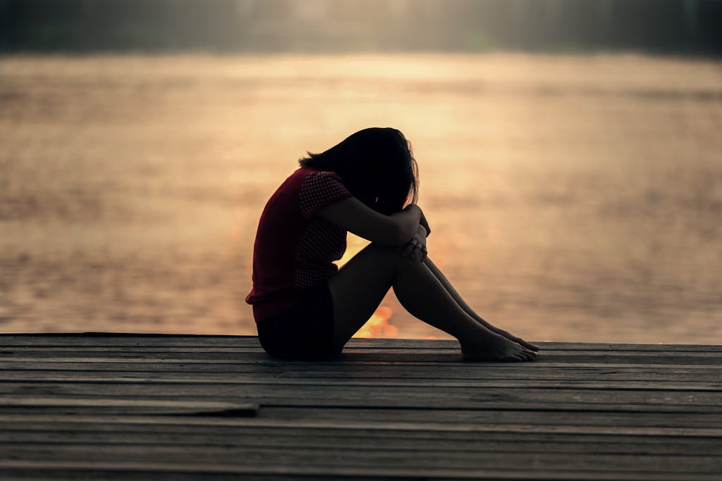 A woman sitting alone on a wooden dock by the lake, wanting to learn how to make friends in your 20s.
