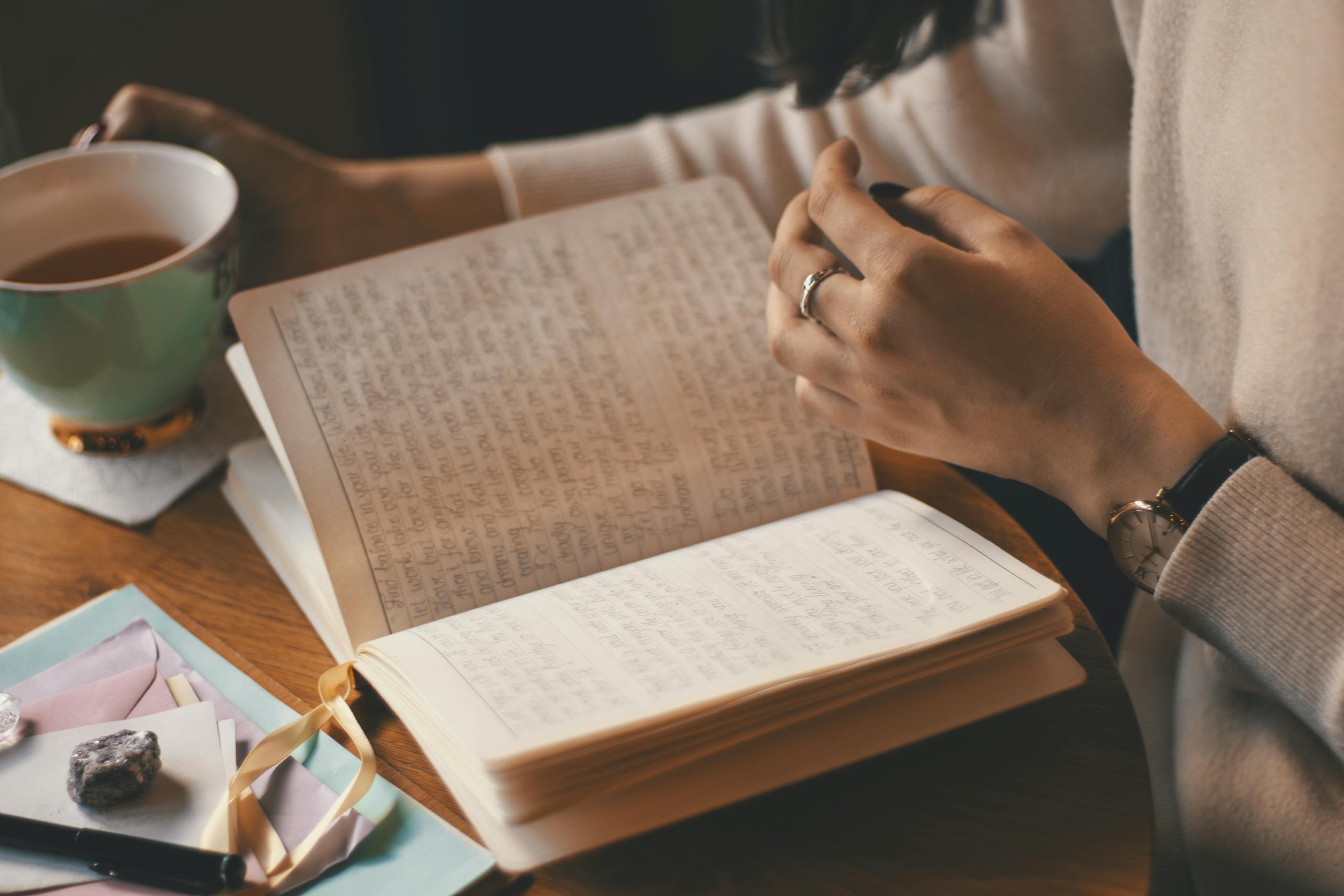 A woman writes in a self-love journal while enjoying a cup of coffee at a wooden table.
