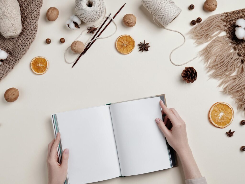 Flat lay of a cozy craft workspace with knitting supplies, dried fruit, and a DIY gratitude joural on a desktop.