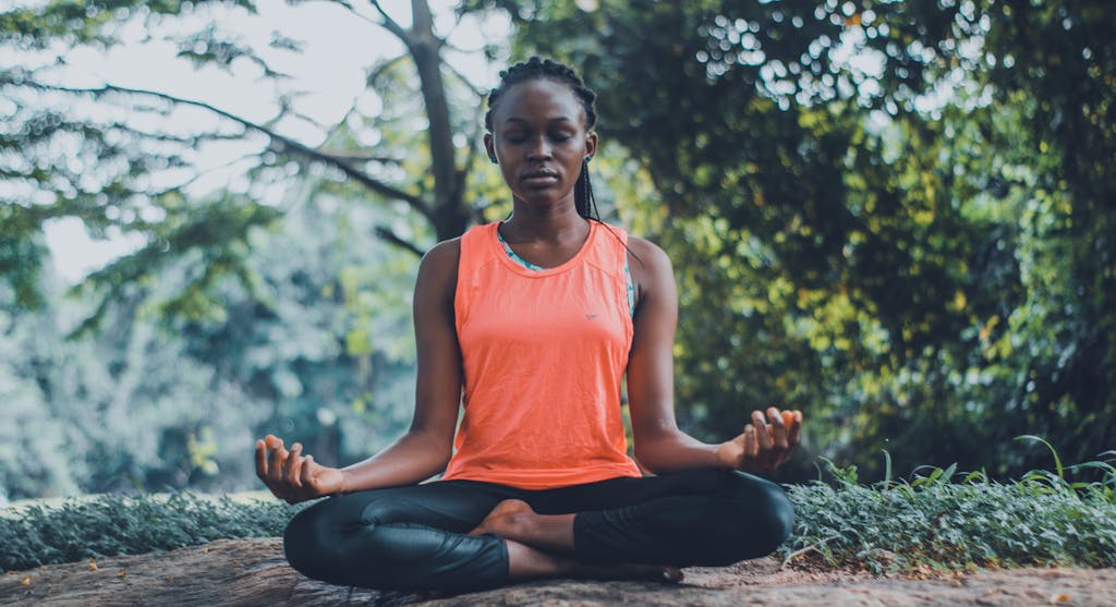 A woman meditating peacefully outdoors in a lush green setting, as part of her 5am morning routine.