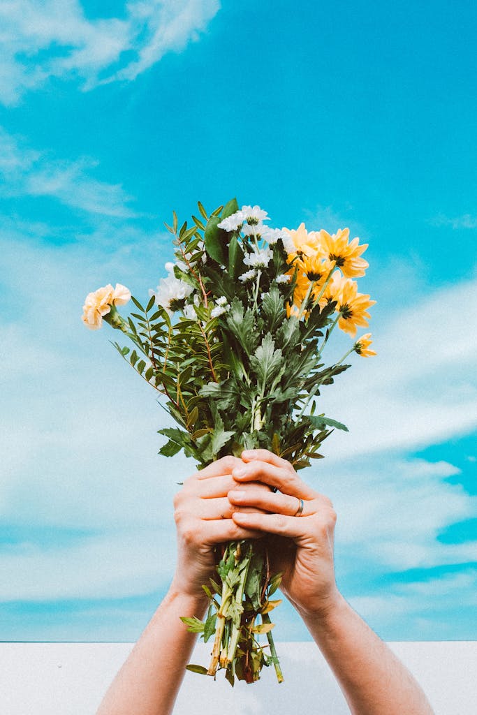 Hands holding a colorful flower bouquet beneath a vivid spring sky.