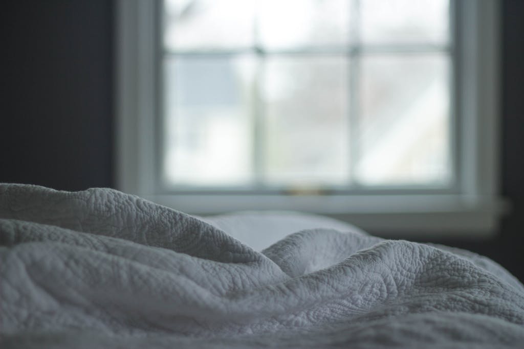 A tranquil bedroom view with a quilted blanket by the window softly lit by morning light, ideal beginning to a sunday reset routine.