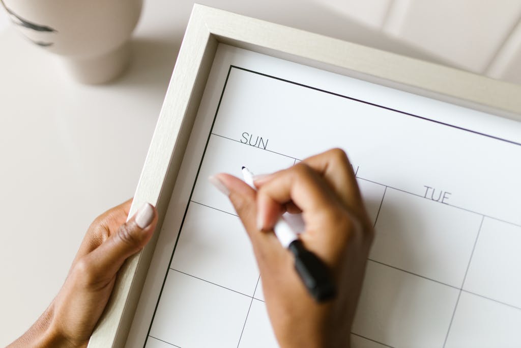 Hands holding a wall calendar, writing with a marker for their sunday reset.